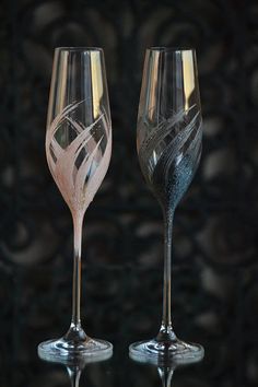 two wine glasses sitting next to each other on top of a glass table with black background