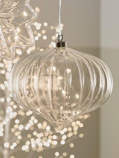 two clear glass ornaments hanging from a chandelier with white lights in the background