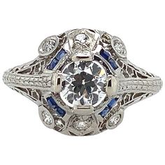 Art Deco platinum filigree ring featuring an European cut diamond weighing .62cts with GIA report. GIA report #2225056999 states H color and I1 clarity. The diamond measures 5.41mm x 5.47mm x 3.29mm. There are 8 specialty caliber French cut synthetic blue sapphire accents measuring about 1.5mm square, some have chips. There are 6 round brilliant cut diamond accents, 4 measure about 2.2mm and 2 measure about 2mm. The ring fits a size 8 3/4 finger and weighs 2.44dwt. It dates from the 1920's. Antique Ring, Silver Flatware, Big Bend, Platinum Engagement Rings, Jewelry Rings Diamond, European Cut Diamonds, Art Deco Diamond, Filigree Ring, Ring Fit