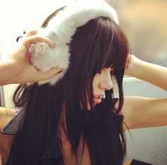 a woman with long black hair is holding her head in the air while wearing a furry hat