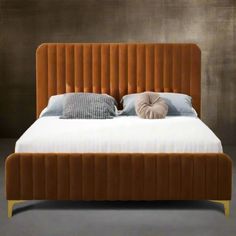 a bed that has some pillows on top of it and is made up with an orange velvet headboard