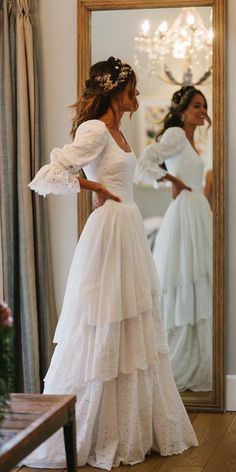 a woman standing in front of a mirror wearing a white wedding dress with ruffles