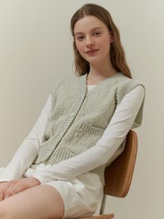 The garment is a sleeveless knitted vest with a V-neckline and front button closure. The knit texture is prominently visible, indicating a cozy, tactile feel. It also features ribbed detailing along the neckline, armholes, and hem, providing a neat and finished look.- The vest includes two front pockets which add practicality and a casual element to the design.- Its relaxed fit suggests it can be layered over various outfits for added warmth.- The ribbed details enhance the fit and contribute to the vest's classic style. Casual Knit Sweater Vest With Button Closure, Casual Knit Vest With Button Closure, Casual Sleeveless Cardigan With Button Closure, Sleeveless Knit Sweater Vest With Buttons, Winter Knit Sweater Vest With Button Closure, Knit V-neck Sweater Vest With Buttons, Sleeveless Knit Vest With Button Closure, Casual Sleeveless Button Cardigan, Sleeveless Knitted Vest