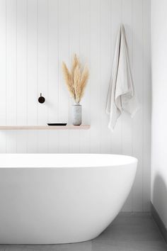 a white bath tub sitting next to a shelf filled with towels and dry grass in a bathroom