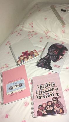 four notebooks are laying on top of a bed with pink flowers and white sheets