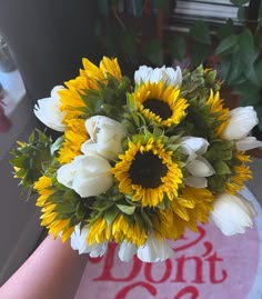 a bouquet of sunflowers and white tulips in someone's hand