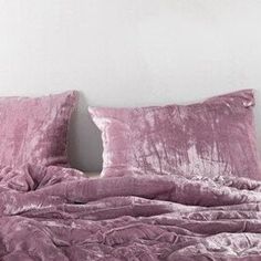 an unmade bed with pink sheets and pillows on top of it in a white room