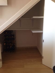 an empty closet under the stairs with wine bottles on shelves and other items in it