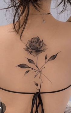 a woman's back with a rose tattoo on her left shoulder and black string