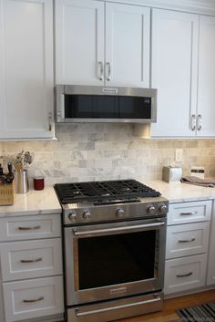 a stove top oven sitting inside of a kitchen next to white cupboards and drawers