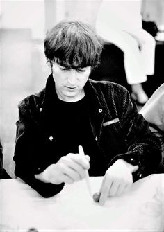 a young man sitting at a table with a pen and paper in his hand, writing