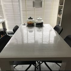 a kitchen table with chairs around it in front of a window that has blinds on the windowsill