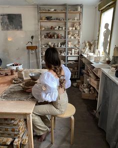 a woman sitting on a chair in a room filled with pottery