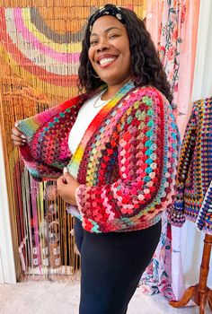 a woman standing in front of a wall with colorful crocheted sweaters on it