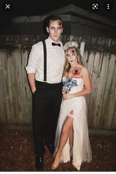 a man and woman dressed up as zombies for a halloween costume party in front of a wooden fence