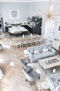 an aerial view of a living room and dining room with wood floors, blue couches, white chairs, and large chandelier