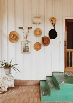 hats are hanging on the wall next to a green step case and potted plant