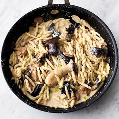 a pan filled with pasta and mushrooms on top of a white marble countertop next to a knife