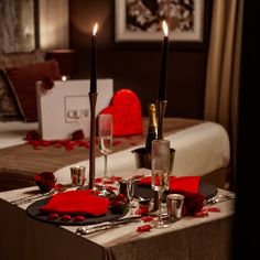 the table is set with two candles and red rose petals on it, along with silverware