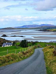 an empty road is shown on the side of a grassy hill with water and hills in the background