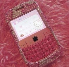 a pink cell phone with hello kitty on the front and back cover sitting on a pink fur surface