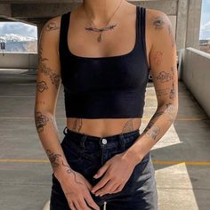 a woman with tattoos on her arms and chest standing in an empty parking lot, looking at the camera