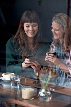 two women sitting at a table looking at their cell phones