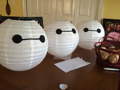 three paper lanterns with faces on them sitting on a table next to a basket full of eggs