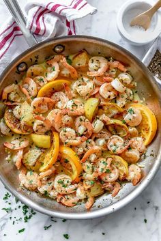 a pan filled with shrimp and squash on top of a white countertop next to a wooden spoon