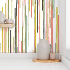 a white vase sitting on top of a counter next to a wall covered in multicolored stripes