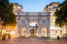 an ornate gate in the middle of a city street at night with trees and buildings behind it