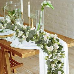 the table is set with white flowers and greenery on it, along with candles