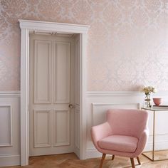 a pink chair sitting next to a white door in a room with wooden floors and wallpaper