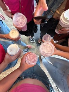 a group of people standing around each other holding drinks and looking at their cell phones