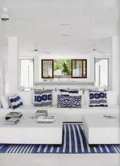 a living room filled with white furniture and blue pillows on top of it's couches