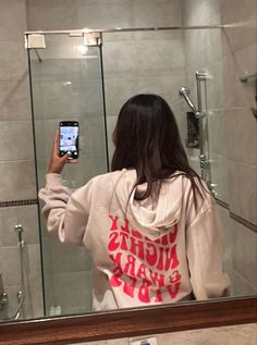 a woman taking a selfie in front of a bathroom mirror while wearing a hoodie