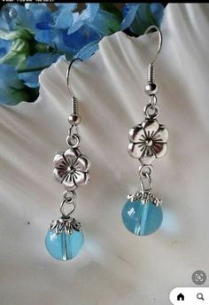 earrings with flowers and blue beads hanging from them on a white table next to a flower