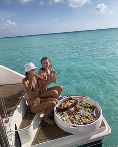 two women sitting on the deck of a boat with food and drinks in their hands