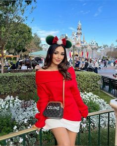 a woman in minnie mouse ears and red sweater posing for the camera with her handbag