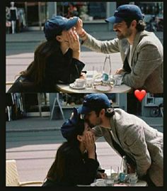 two people sitting at a table and one is kissing the other