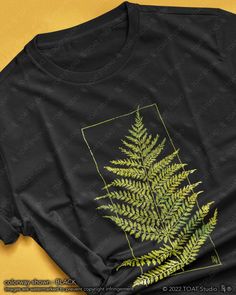 a black t - shirt with a green fern leaf on the front and yellow background