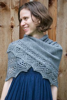 a woman wearing a shawl standing in front of a wooden fence