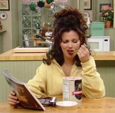 a woman sitting at a table in front of a coffee cup and reading a magazine