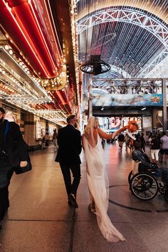 a bride and groom walking through an indoor mall at night with lights on the ceiling