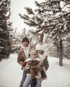 two adults and a child are standing in the snow near a pine tree with snow falling all around them