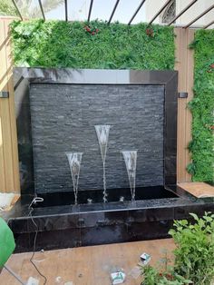 an outdoor fireplace with three glass vases on it's side, surrounded by greenery