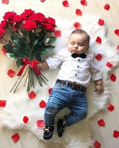 a baby laying on top of a white rug next to red roses