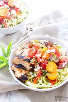 two bowls filled with pasta and vegetables on top of a white cloth next to silverware