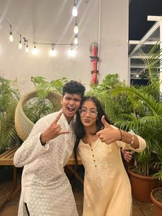 two people standing next to each other in front of potted plants and giving the thumbs up sign