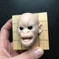 a hand holding a small doll head on top of a piece of wood with eyes